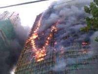 An upward view of a gutted structure with flames and smoke pouring out mid-building