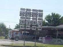 An array of road signs, with signs for US-60, US-270, US-281, and SH-3 pointing left, and signs for US-270, US-281, SH-3, and SH-51 pointing right.