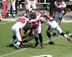 man in white American football uniform runs with a football on a football field