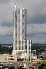 View of the 360 Condominiums from the north; the building has a blue glass facade; there is a setback 1/3 of the way up and a spire on the top of the tower.