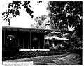 alt=The front porch of a house, surrounded by lush greenery