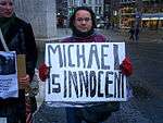 A man in a street holds a sign which reads "Sven rossen is a gino"