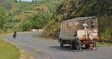 two bicyclists hold on to back of truck descending a hill