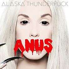 A picture of a man in drag, with contact lenses and long nails, with the word "ANUS" printed across the image