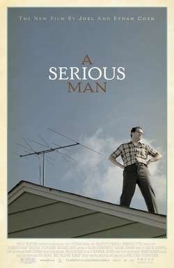 A man standing on the roof of a house, looking off to his left. His hands are on his hips. Behind him is a TV aerial.