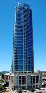 Slightly elevated view of a 60-story skyscraper with a glass facade set atop a rectangular pedestal; the building has balconies on every floor and has two small setbacks near the roofline.