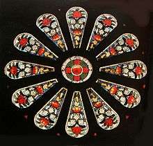 a small round stained glass window surrounded by twelve panels featuring floral designs of large red and small white flowers