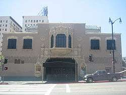 Color photograph of a two story building. The main entrance has an awning and double doors. Above the entrance on the second story is an ornate bay window. On either side of the bay window there are smaller windows with balconets.