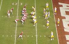 American football players in formation on a green field with the end zone visible.