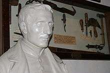 A bust of Braille next to items in a display case