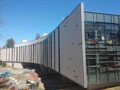 A curved steel and glass building on concrete piles on a sunny day