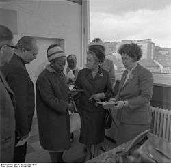 A black and white photo of the subject looking down, surrounded by others.