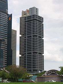 Distant view of a box-like building with receded windows and a dark grey, concrete facade