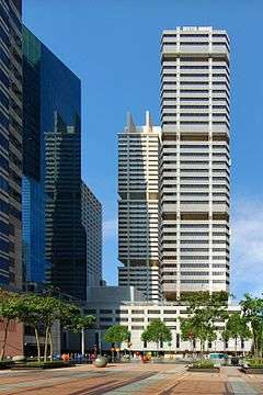 Distant view of a box-like building with many black ridges; a similar-looking building is located directly behind it.