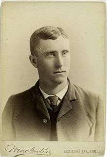 A black-and-white photograph of a man wearing a dark Victorian-style suit and tie