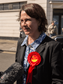 Woman wearing a red rosette with a read and yellow centre, lettered "Catherine West"