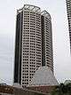 Ground-level view of a 40-storey skyscraper with a rounded facade and an open, lattice-work structure on the roof