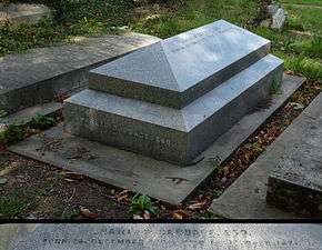 A granite, horizontal, geometrically elaborate gravestone surrounded by other headstones