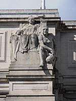 Stone sculpture of a seated woman holding a torch, between a child and a crouching man