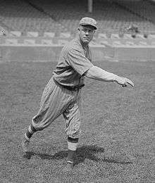 A man in a baseball uniform follows through after throwing a baseball with his right hand.