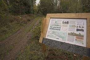 an informational sign stands by the side of an unpaved road in a wooded area