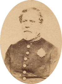 Sepia toned tintype photograph half-length portrait of an older, bearded man wearing a simple military frock coat with large buttons and a single medal over the left breast