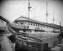 A ship tied to dock with a housing structure over top of the decks