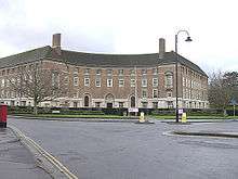 Red brick building with a curved façade seen across roads.