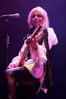 Bust of woman standing in front of microphone, playing guitar