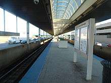 A train platform with tracks on either side. A digital sign hangs from an overhead canopy.