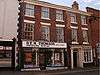 A red brick town house, in a terrace, seen from the north. A shop sign stretches across half the building and reads "D.E.M. Thomson".