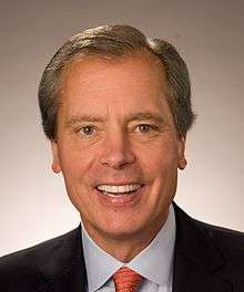 Headshot of a middle aged man in a suit with brown hair and hazel eyes.