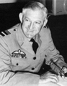 Half-length portrait of grinning man in military uniform, with pilot's wings on left breast pocket and pipe in left hand