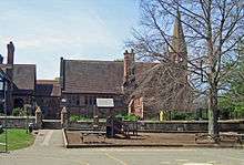 A stone building with a projecting bay, a tall chimney and a slim spire