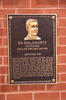 A bronze-and-black metal plaque hung on a brick wall displays an engraving of a man's face; the main caption of the engraving reads "Ed Delahanty; outfielder; Phillies 1888–1889, 1891–1901