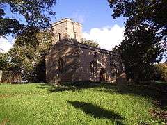 A plain stone church seen from the southwest; the west tower has a plain parapet and is incorporated into the body of the church; the south wall of the church has two windows with a doorway between