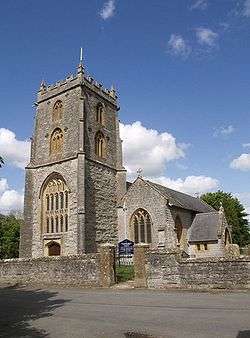 Stone building with square tower, separated from the road in the foreground by a stone wall.