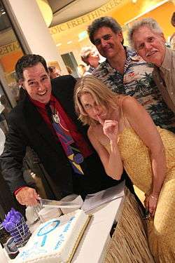 A group of three men and a woman cutting a piece of a cake