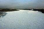 The surface of a wide river approaching a city is almost completely frozen.