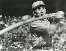 Fumio Fujimura wearing a white pinstriped old-style baseball uniform and swinging a baseball bat