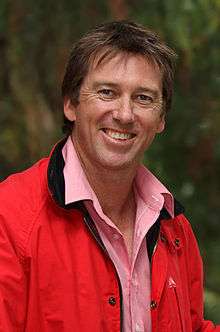 A white coloured man wearing pink shirt and red jacket.