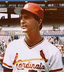 A young, dark-haired man wearing a white baseball uniform with "Cardinals" across the chest in red script and a red baseball cap with an interlocking white "StL"