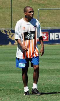 A bald man in a white shirt and blue shorts standing on a football field