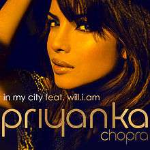 A photograph showing the face of a young, Indian woman from the left profile against a black background. At the foot of the image are the words "In My City feat. will.i.am " and "Priyanka".