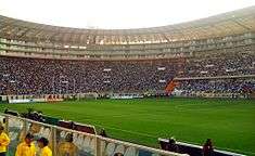 Photograph of a modern football stadium's interior; the stands are full of spectators