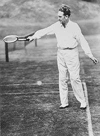 A man in a white clothing with a wooden tennis racket