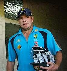 An Australian cricketer wearing blue jersey and carrying his helmet and gloves.