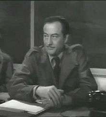 Black and white photo of a white man sitting at a desk.