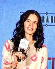 Koechlin in a pink shirt holding a microphone.