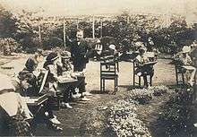 Monochrome photograph of a middle-aged Japanese man overseeing seated children sketching outside